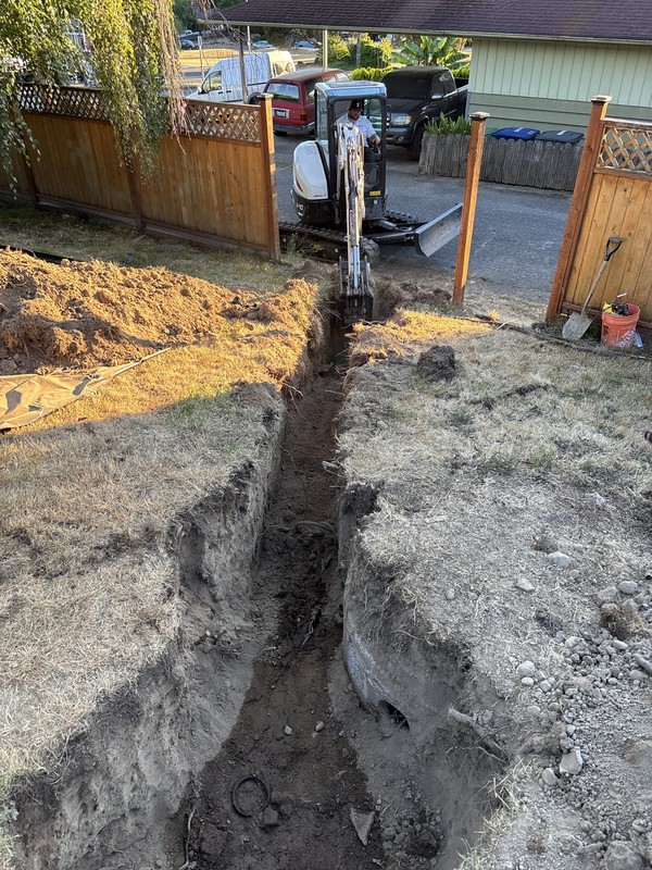 Bee's Plumbing technician operating a mini excavator to dig the sewer trench alongside a Seattle, WA home