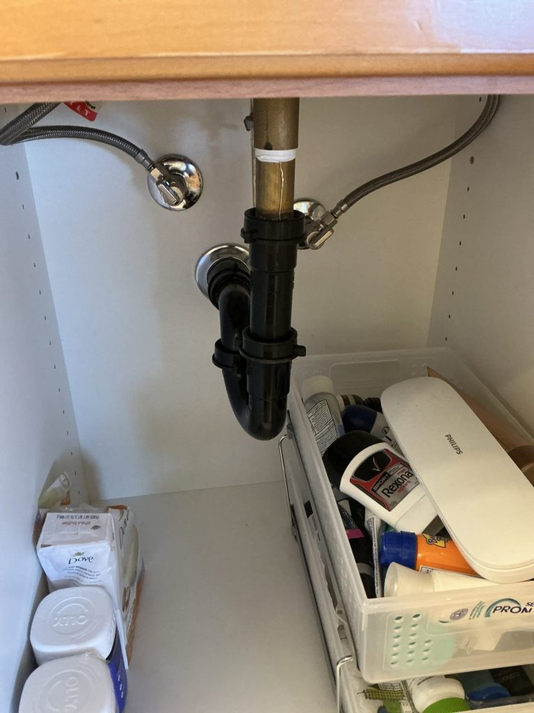 The existing black P-trap and brass tailpiece under the bathroom vanity before the drain was opened up
