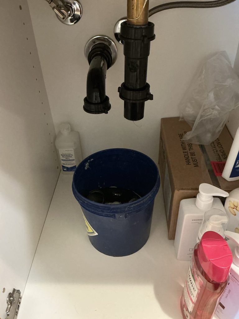 P-trap removed and a bucket set underneath to open access to the bathroom sink drain line